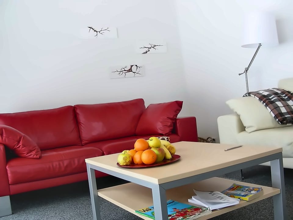 Wohnzimmer mit rotem Ledersofa, Couchtisch mit Obstschale und Stehlampe