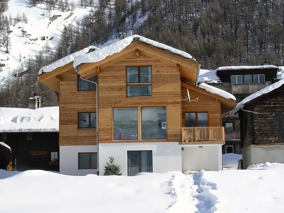 Chalet Adlerhorst mit Holzbalkon und schneebedecktem Dach vor dem Walliser Dorfkern im Winter